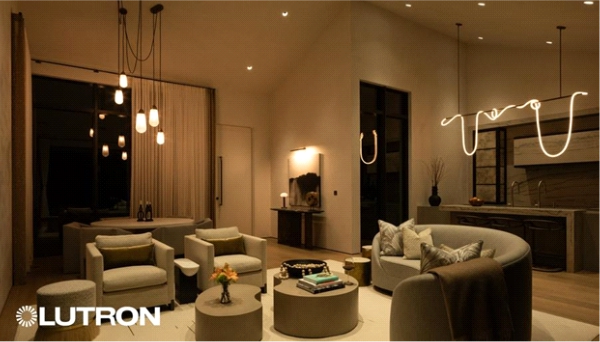 A modern open-concept living room and kitchen with warm, layered lighting, featuring pendant lights, recessed ceiling lights, cozy seating areas, and a Lutron lighting system creating a soft, ambient evening atmosphere.