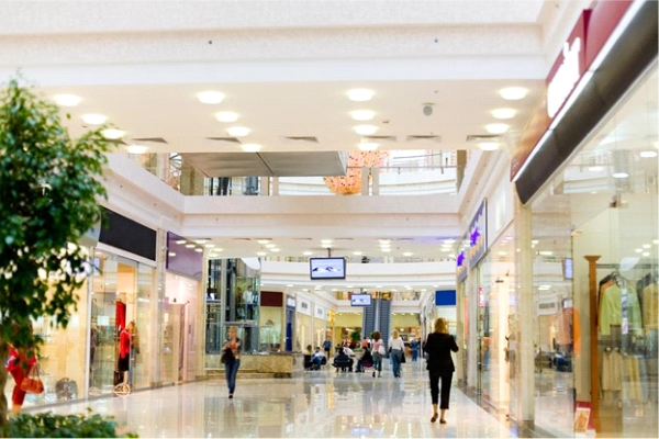 Indoor shopping mall with digital signage displays and people walking through retail corridor.
