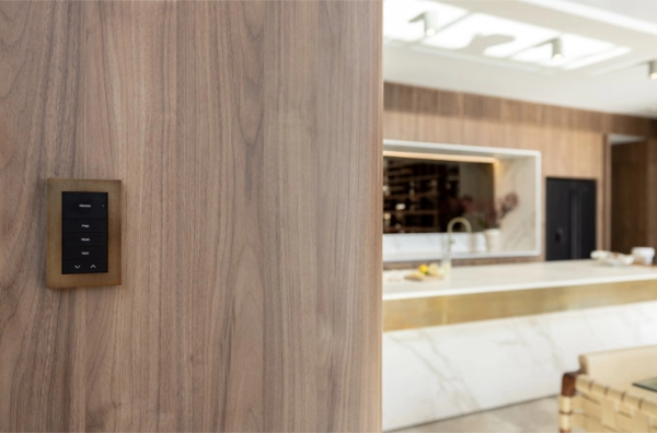Brushed brass Control4 keypad on a wood panel controls lighting scenes in a high-end kitchen with marble and gold finishes.