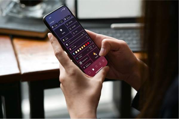 A person using a smartphone to the Control4 app, adjusting lighting, climate, and entertainment settings through a modern, dark-themed interface.