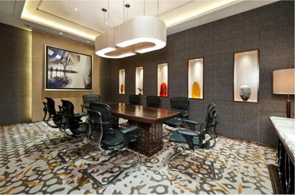 A modern conference room with a long wooden table, ergonomic office chairs, sculptural pendant lighting, and recessed display niches, showcasing a well-designed corporate meeting space.